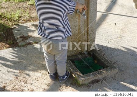 公園の水飲み場で蛇口をひねる子供の後ろ姿 公園の水飲み場で蛇口をひねる子供の後ろ姿 139610343