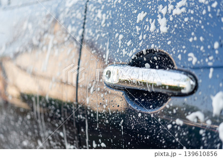 Closeup of car door covered with soap foam during vehicle washing process showing glossy surface cleaning and automotive maintenance detail Closeup of car door covered with soap foam during vehicle washing process showing glossy surface cleaning and automotive maintenance detail 139610856