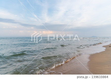 Peaceful ocean waves reaching sandy beach under soft cloudy sky creating relaxing tropical coastal landscape and natural seaside atmosphere 139610864