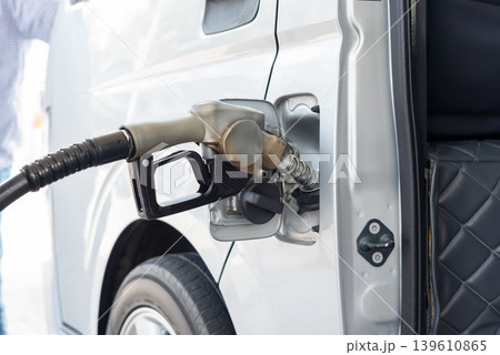 Closeup of fuel nozzle pumping gasoline into white van during vehicle refueling process at service station with transportation energy concept Closeup of fuel nozzle pumping gasoline into white van during vehicle refueling process at service station with transportation energy concept 139610865