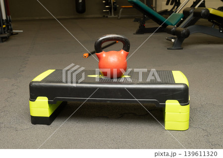 Kettlebell on aerobic step in gym setting with exercise equipment in background Kettlebell on aerobic step in gym setting with exercise equipment in background 139611320