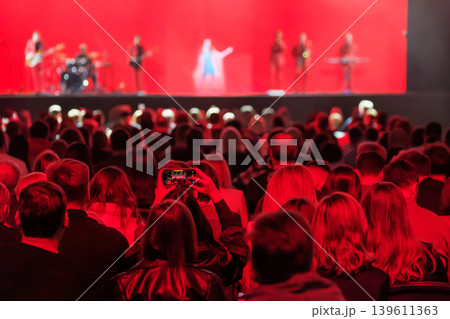 Concert audience watching live band on stage, crowd recording performance under red lights Concert audience watching live band on stage, crowd recording performance under red lights 139611363