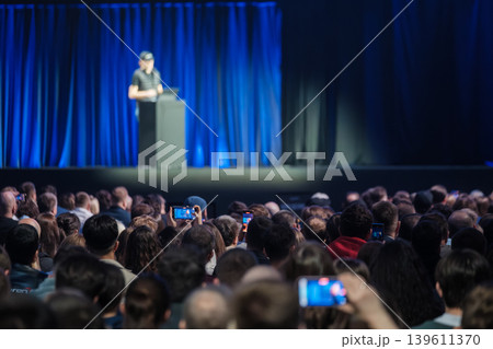 Audience recording speaker on stage at technology conference, crowd watching live presentation Audience recording speaker on stage at technology conference, crowd watching live presentation 139611370