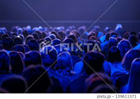 Audience watching stage under blue lighting, large seated crowd at concert or theater event 139611371