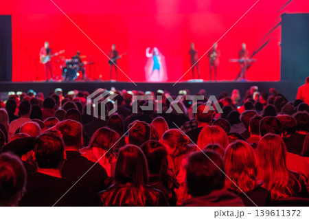 Crowd watching live music concert on stage with band and red lighting, audience enjoying show 139611372