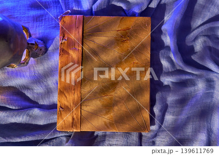 Sunlit ridges highlight handcrafted leather binding. Tactile details and handstitched spine on blue drape surface Sunlit ridges highlight handcrafted leather binding. Tactile details and handstitched spine on blue drape surface 139611769