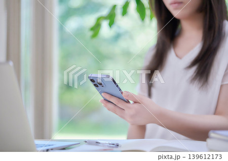 スマートフォンを見ながら勉強する若い女性 スマートフォンを見ながら勉強する若い女性 139612173