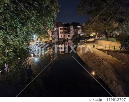 Phone photo of the Petite France area in Strasbourg at night, showing a picturesque river view. Scenic urban scene with historic half-timbered houses, reflections, and charming evening atmosphere. Phone photo of the Petite France area in Strasbourg at night, showing a picturesque river view. Scenic urban scene with historic half-timbered houses, reflections, and charming evening atmosphere. 139612707