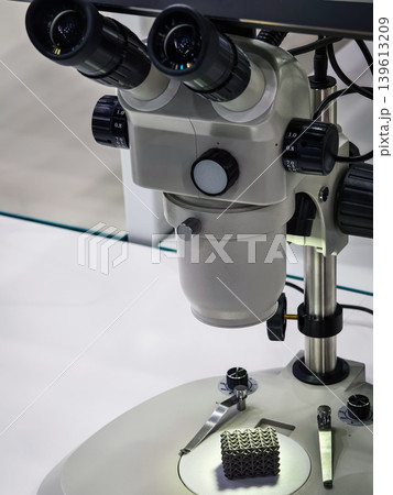 Microscope used for examining small objects in a laboratory setting with focus on a textured sample underneath Microscope used for examining small objects in a laboratory setting with focus on a textured sample underneath 139613209