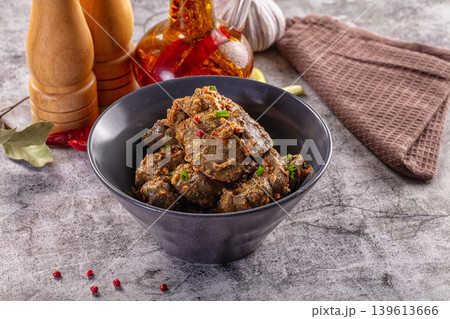 liver with spices and green onions in a dark bowl on a textured stone table. 139613666