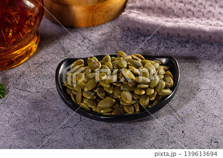 A small black bowl of healthy shelled pumpkin seeds or pepitas on a rustic grey tabletop A small black bowl of healthy shelled pumpkin seeds or pepitas on a rustic grey tabletop 139613694