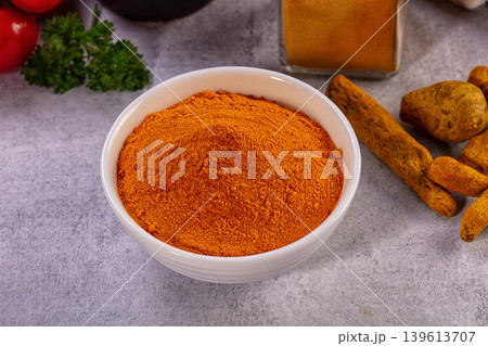 Bright turmeric powder in white bowl with fresh spices and vegetables 139613707