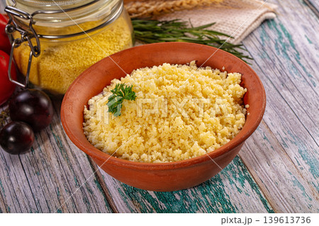 Cooked couscous in rustic clay bowl with fresh tomatoes and herbs on wooden table 139613736