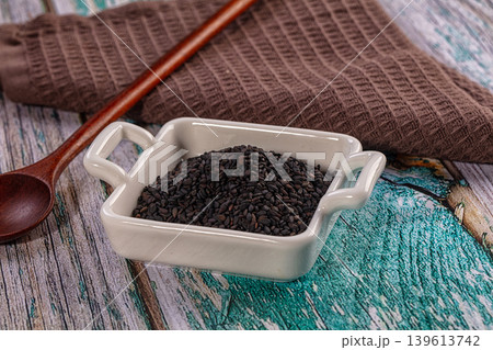 Black sesame seeds in white ceramic bowl with wooden spoon on rustic table Black sesame seeds in white ceramic bowl with wooden spoon on rustic table 139613742