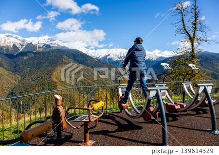 Man exercises on outdoor gym equipment with mountains in background Man exercises on outdoor gym equipment with mountains in background 139614329