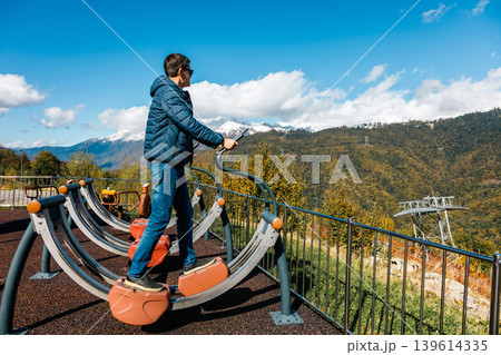 Man uses outdoor fitness equipment to exercise on mountain overlook 139614335