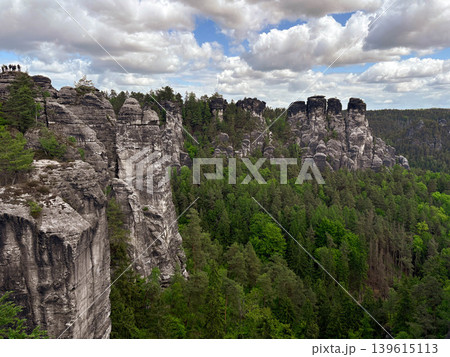 a stunning natural landscape dominated by massive, weathered sandstone rock pillars rising dramatically from a dense green forest. Saxon Switzerland in Germany. 139615113