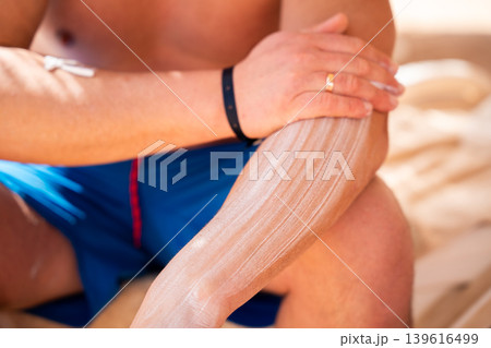 Caucasian man applying sunscreen cream on forearm while sitting on a beach during a summer vacation at a seaside resort. Sun protection and skincare routine Caucasian man applying sunscreen cream on forearm while sitting on a beach during a summer vacation at a seaside resort. Sun protection and skincare routine 139616499