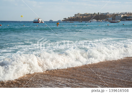 Sea waves on a sandy beach in Sharm El Sheikh on the Red Sea coast with boats and resort buildings in Egypt. Summer travel and seaside tourism Sea waves on a sandy beach in Sharm El Sheikh on the Red Sea coast with boats and resort buildings in Egypt. Summer travel and seaside tourism 139616508