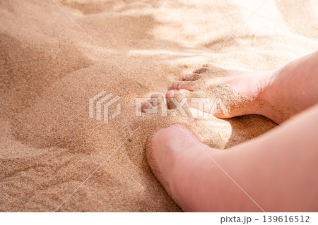 Bare feet covered with warm beach sand during summer vacation on seaside coast under bright sunlight. Relaxation and wellness lifestyle 139616512