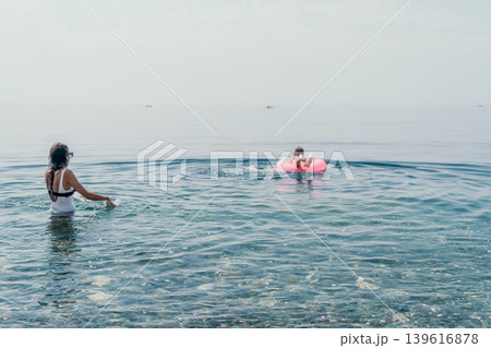 Swimming ocean vacation woman in white swimsuit and sunglasses enjoys a sunny day at the sea with a person on a pink inflatable ring Swimming ocean vacation woman in white swimsuit and sunglasses enjoys a sunny day at the sea with a person on a pink inflatable ring 139616878