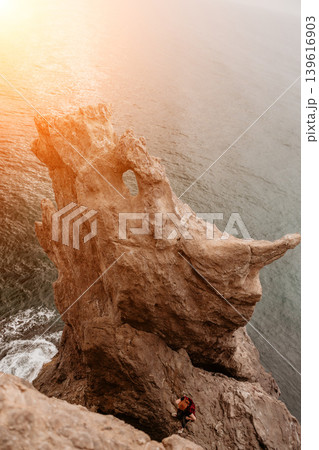 Cliff Sea Coast vertical rock formation standing against the ocean at sunrise with a lone traveler below 139616903
