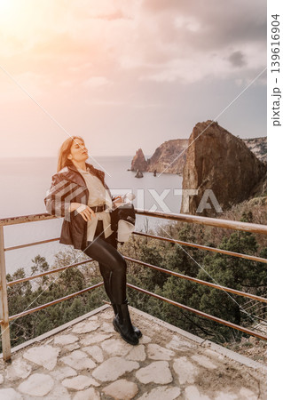 Woman Coastal Sunset enjoying the breathtaking sea view from a rocky cliff platform during a peaceful golden hour trip 139616904