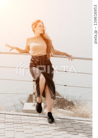 Woman ginger coastline leaning on a metal railing at a sea viewpoint during a bright sunset enjoying the outdoor scenery Woman ginger coastline leaning on a metal railing at a sea viewpoint during a bright sunset enjoying the outdoor scenery 139616953
