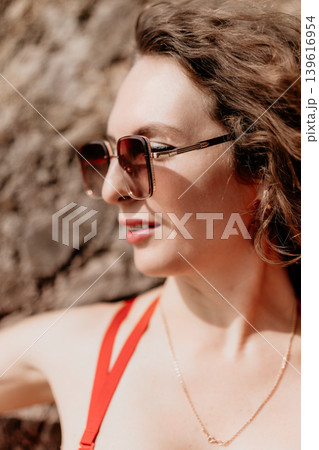 Woman Sunglasses Swimwear woman in stylish shades and red bikini posing against textured rock wall on sunny summer day Woman Sunglasses Swimwear woman in stylish shades and red bikini posing against textured rock wall on sunny summer day 139616954
