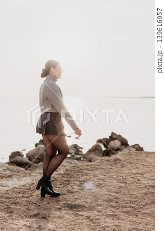 Woman shoreline fashion walking along a rocky coast at sunset wearing a stylish sweater and skirt with copy space Woman shoreline fashion walking along a rocky coast at sunset wearing a stylish sweater and skirt with copy space 139616957