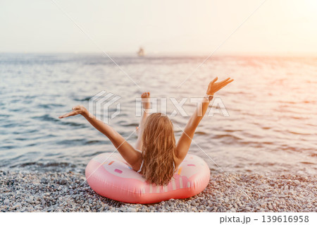 Woman, beach, sea. Young woman relaxes on inflatable ring at pebble beach, enjoying golden hour. Woman, beach, sea. Young woman relaxes on inflatable ring at pebble beach, enjoying golden hour. 139616958