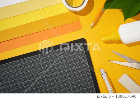 Craft supplies for paper crafts and a cutting mat on a yellow background. Glue, scissors, a pencil, and sticky tape. Copy space. Craft supplies for paper crafts and a cutting mat on a yellow background. Glue, scissors, a pencil, and sticky tape. Copy space. 139617640