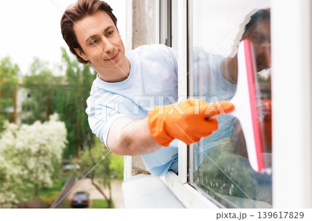 A man in orange gloves uses a squeegee to wash a window. This bright image illustrates spring cleaning, home maintenance, and domestic chores 139617829