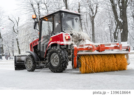 City street cleaning vehicle with rotating brush . Tractor removing snow from sidewalk with brush and steel blade 139618664