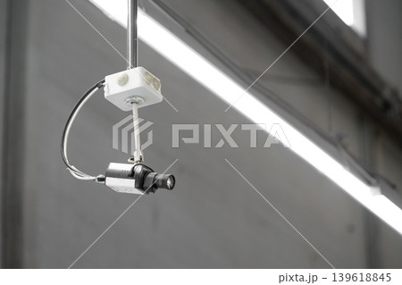A ceiling-mounted surveillance camera installed on a metal conduit inside an industrial or commercial interior. Copy space 139618845