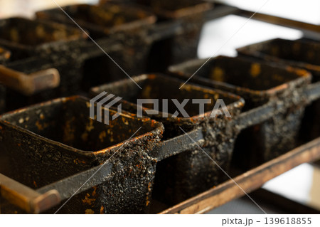 Close-up of a well-used industrial metal bread baking pan with multiple rectangular molds, showing heavy patina, baked-on residue, and signs of long-term use. 139618855