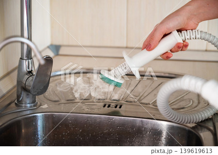 Cleaning the kitchen surface with a steam cleaner next to the sink at home Cleaning the kitchen surface with a steam cleaner next to the sink at home 139619613