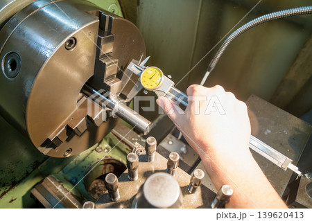 High angle shot of a skilled machine operator measuring a metal shaft part with a precision dial vernier caliper. High angle shot of a skilled machine operator measuring a metal shaft part with a precision dial vernier caliper. 139620413