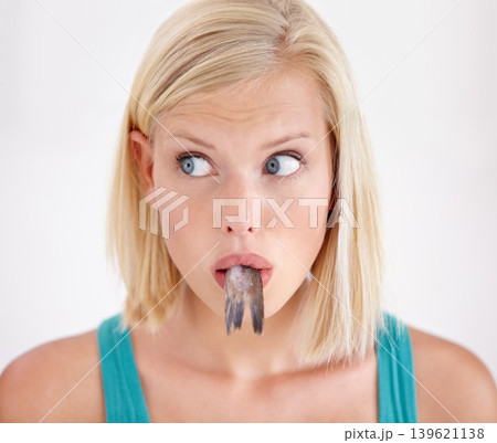 Face, woman and eating tail of fish with surprise and shock on white background of studio. Crazy, diet and person with taste of weird seafood, cuisine and confused with gross or strange food in mouth Face, woman and eating tail of fish with surprise and shock on white background of studio. Crazy, diet and person with taste of weird seafood, cuisine and confused with gross or strange food in mouth 139621138