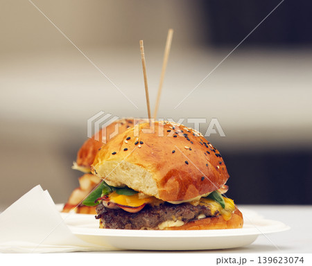 Two gourmet bacon cheeseburgers placed on table at food festival Two gourmet bacon cheeseburgers placed on table at food festival 139623074