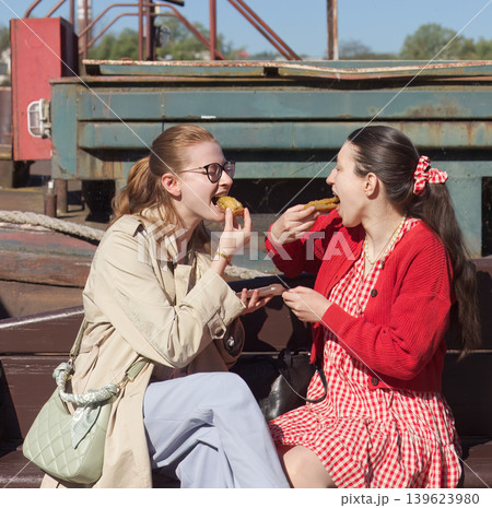Two smiling friends eating street food at outdoor farmers market Two smiling friends eating street food at outdoor farmers market 139623980