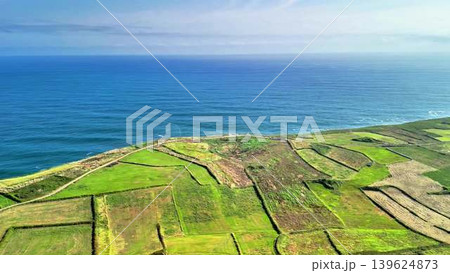 Stunning Aerial View of Coastal Cliffs and Lush Green Fields Under a Bright Blue Sky 139624873