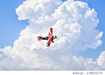 A red aerobatic biplane performing air shows in a blue sky with white clouds. Classic airplanes A red aerobatic biplane performing air shows in a blue sky with white clouds. Classic airplanes 139625274