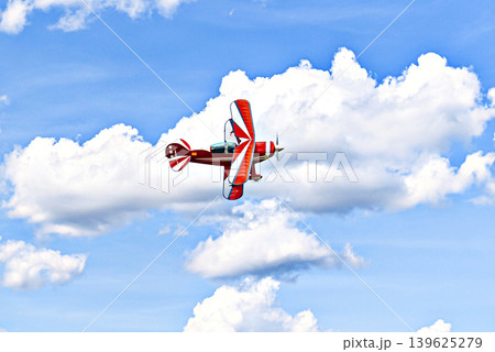 A red aerobatic biplane performing air shows in a blue sky with white clouds. Classic airplanes A red aerobatic biplane performing air shows in a blue sky with white clouds. Classic airplanes 139625279