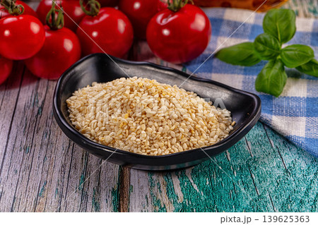 Culinary ingredients, sesame seeds in black bowl, vibrant cherry tomatoes, basil leaf, rustic wooden background Culinary ingredients, sesame seeds in black bowl, vibrant cherry tomatoes, basil leaf, rustic wooden background 139625363