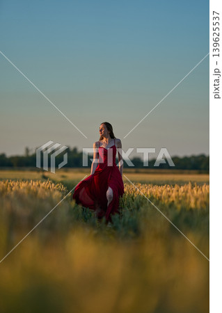 Woman rye field red dress. Happy woman in a long red dress in a beautiful cornfield. Old caste ruins in the background Woman rye field red dress. Happy woman in a long red dress in a beautiful cornfield. Old caste ruins in the background 139625537
