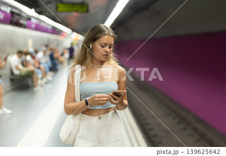 Girl with earphones and phone is standing on subway platform Girl with earphones and phone is standing on subway platform 139625642