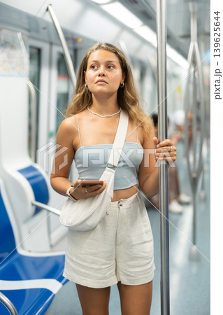 Young woman with phone standing in metro car Young woman with phone standing in metro car 139625644