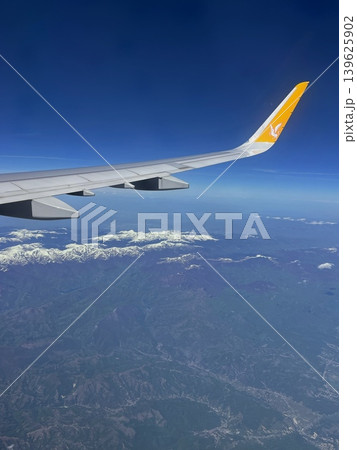 Airplane wing with orange tip above snow-capped mountains and clear blue 139625902