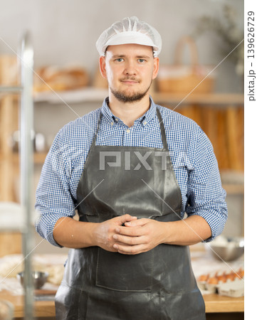 Male baker stands near work table in bakery, resting while working. Male baker stands near work table in bakery, resting while working. 139626729